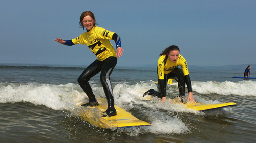A photo of two teenagers surfing in shallow waters is visible
