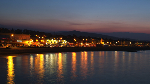 A picture from distance of a harbor late at night with lights shining on seafront